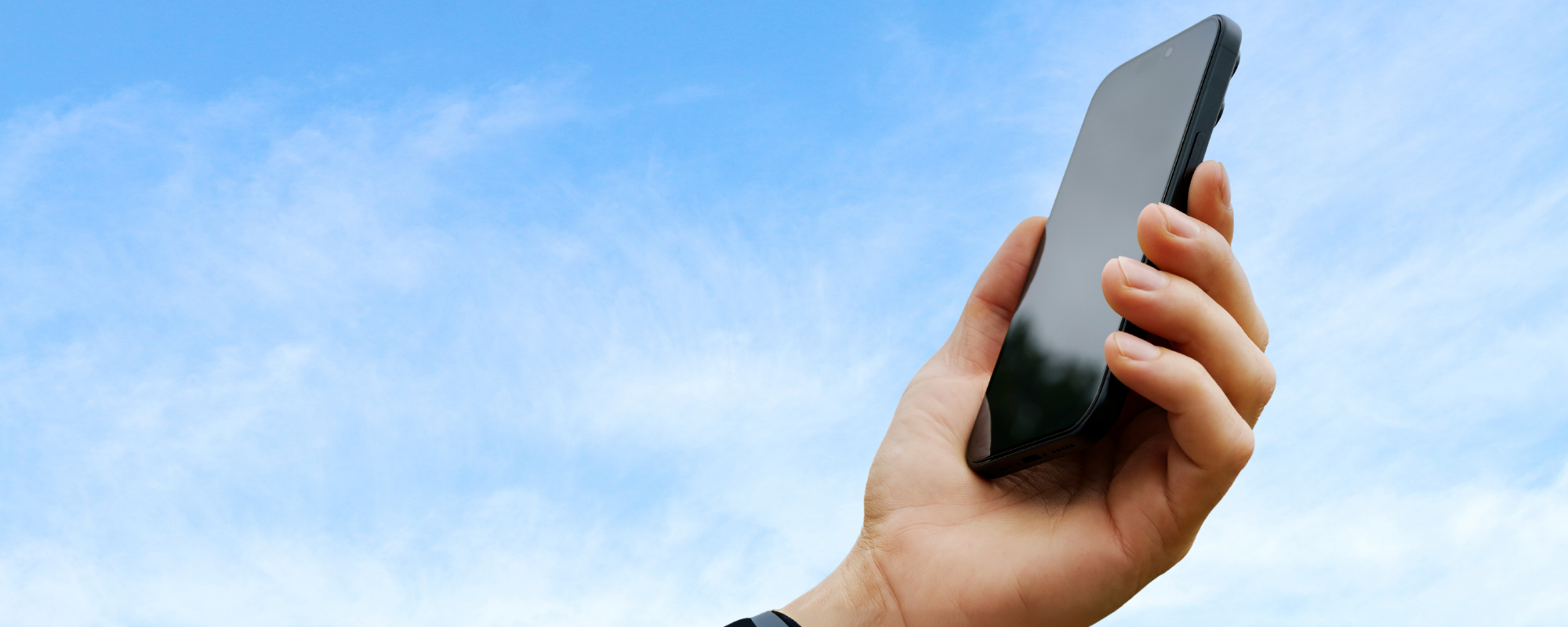Hand holding a smartphone against a blue sky