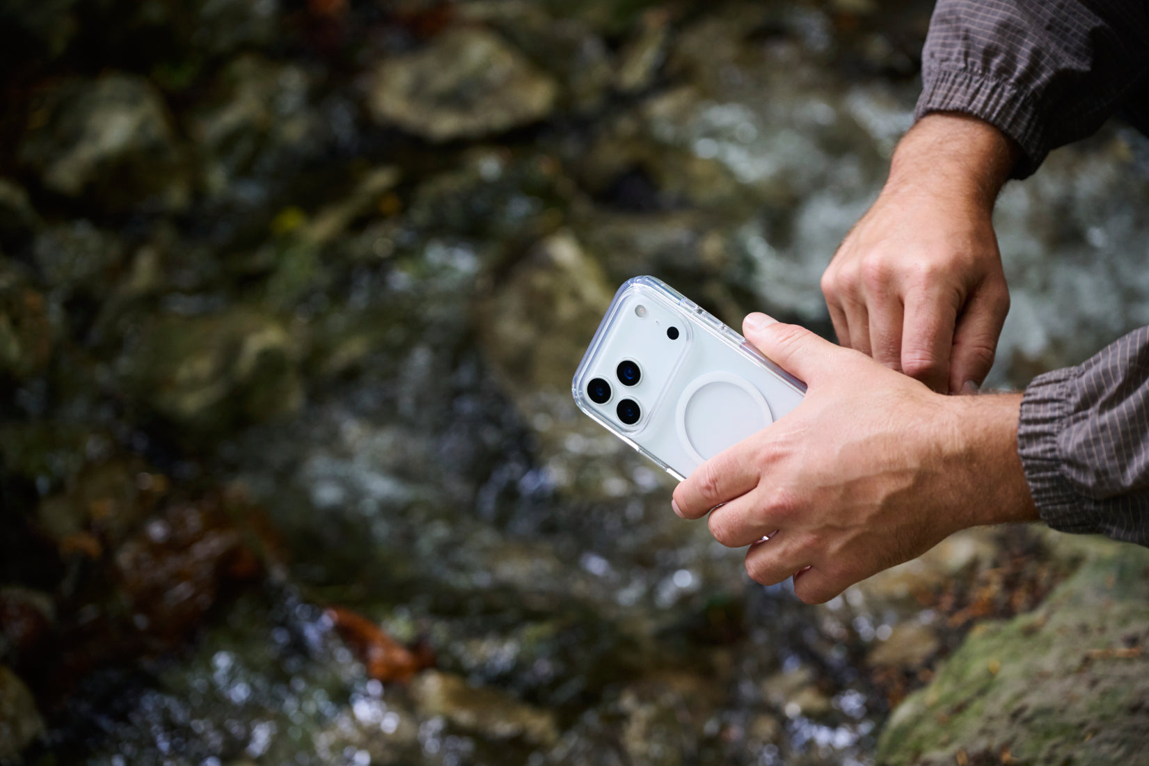Person holding a smartphone with a water droplet on the screen against a natural background
